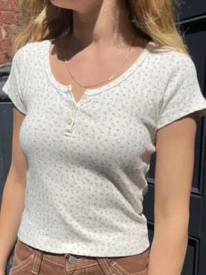 Brandy Melville blommig topp (Zelly) - Söt och trendig topp från Brandy Melville i den populära Zelly-modellen. Samma modell som på bilden (original från hemsidan), men med gröna blommor istället för rosa.  Vit med små gröna blommor och knappar framtill – perfekt till jeans eller kjol för en clean och “Brandy aesthetic” look.  Använd men i fint skick! Inga hål eller större slitningar, bara normalt använd.  Superfin passform som sitter tajt och stretchigt.