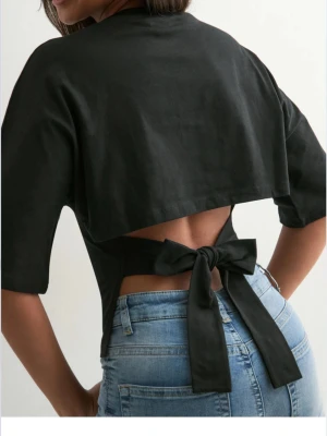 Svart bolerotopp med knyt i ryggen - Trendig svart topp med öppen rygg och knytning bak. Toppen har korta ärmar och croppad passform som ger en bra passform. 