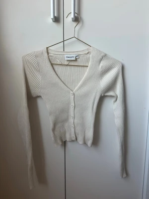 Vit ribbad kofta från Kappahl - Säljer en vit ribbad kofta från Kappahl med v-ringning och knäppning framtill. Koftan har långa ärmar och är tillverkad i ett mjukt, stretchigt material som sitter snyggt på kroppen. Storlek XS men liten i storleken. Aldrig använt
