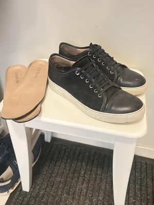 Marinblå Lanvin sneakers i läder - Stilrena marinblå sneakers från Lanvin med ovandel i läder och mocka, vita gummisulor och svarta skosnören. Klassisk låg modell med rund tå och utbytbara innersulor i beige läder. Perfekta för en clean och tidlös look.