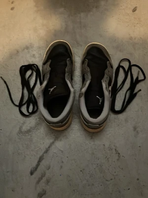 Svarta och vita Air Jordan sneakers - Säljer ett par klassiska Air Jordan sneakers i svart och vitt med ikoniska Jumpman-loggan på plösen. Skorna har en låg silhuett och är tillverkade i en kombination av läder och textil. Svarta skosnören medföljer. Perfekta för dig som gillar streetwear och sportig stil.