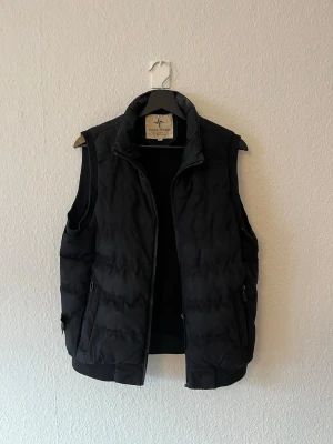 Svart dunväst från Stone Island - Vintage Stone Island väst från 90-talet. Storlek sitter som en M. Säljes billigt då den är för liten för mig. Defekter finns då dragkedjan behöver en ny ”krok” själva zipen fungerar men den behöver en ny krok för att kunna användas, även innerfickan är uppriven inget som syns från utsidan dock.