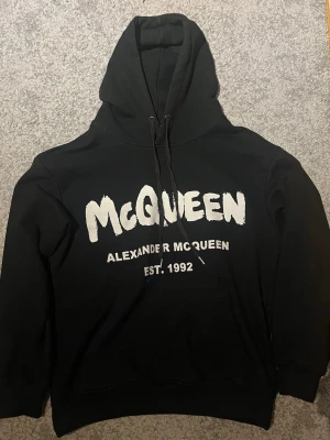 Svart hoodie från Alexander McQueen - Svart hoodie från Alexander McQueen med stor vit mcqueen logga framtill. Tillverkad i mjukt bomullsmaterial, perfekt för en avslappnad streetwear-look.                     Priset Kan diskuteras vid snabb affär Storlek M men kan sitta som S