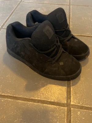 Svarta DC Shoes sneakers - Svarta sneakers från DC Shoes i klassisk skate-modell. Sulan är i gummi och skon har diskret DC-logga på sidan. Perfekta för dig som gillar streetwear och skate.