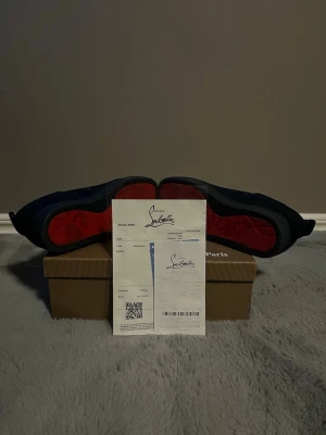 Christian Louboutin svarta sneakers - Snygga svarta sneakers från Christian Louboutin med ikonisk röd sula. Skorna har en låg siluett, svarta skosnören och är tillverkade i ett lyxigt material som ger en exklusiv känsla. Perfekta för dig som vill sticka ut med stilrena detaljer och premiumkänsla.