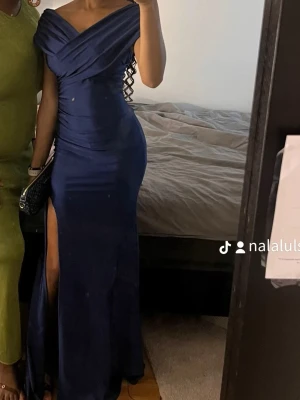  Fashion nova Marinblå långklänning offshoulder - Säljer en elegant marinblå långklänning med offshoulder-design och draperad överdel. Klänningen har en hög slits på sidan och figurnära passform som framhäver siluetten. Perfekt för bal eller festkvällar. Materialet känns mjukt och följsamt.