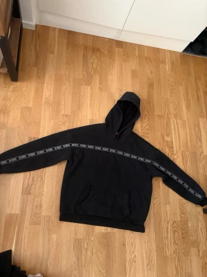 Svart hoodie Guess  - Säljer en svart hoodie från Guess med stor huva och magficka. Snygg detalj med vit GUESS-logga längs bröstet och armarna. 