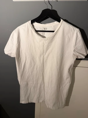 Vit basic t-shirt från 157 - En enkel vit t-shirt från 157 med rund hals och korta ärmar. Tillverkad i mjuk bomull och har en klassisk passform som funkar till allt. Perfekt att styla med jeans eller shorts för en clean look.