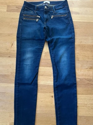 Skinny jeans - Snygga mörkblå skinny jeans med fyra dragkedjor framtill som cool detalj. Klassisk femficksmodell med två bakfickor och knappgylf. Jeansen har en smal passform och är tillverkade i stretchigt denimtyg för extra komfort.