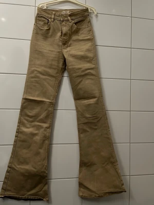Beiga bootcut jeans pull&bear - Säljer ett par snygga beiga bootcut jeans från Lee. Jeansen har hög midja, klassiska fem fickor och utsvängda ben. Tillverkade i ett mjukt bomullsmaterial med en liten Lee-logga på bakfickan. Perfekta för dig som gillar retrostil och vill sticka ut.