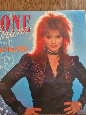 Vinylsingel Stranded/Secrets of a Heart - Säljer en vinylsingel med låtarna 'Stranded' och 'Secrets of a Heart'. Omslaget har en person med rött hår och svart spetsblus mot blå bakgrund. Text i rött och orange. Perfekt för dig som gillar retro och samlar på vinyl.