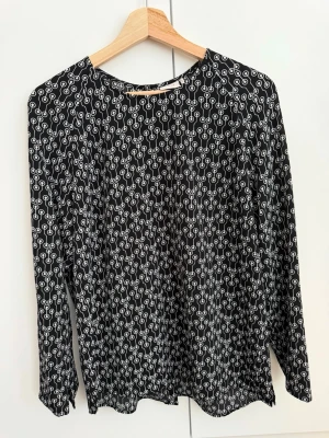 Dobber - Svart blus med vitt mönster - Snygg svart blus med vitt grafiskt mönster. Blusen har lång ärm och lös passform, perfekt för en trendig och avslappnad stil. Materialet känns lätt och luftigt, vilket gör den skön att bära hela dagen. Passar till både jeans och kjol.