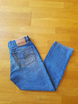 Levi's 505 blå raka jeans - Klassiska blå Levi's 505 jeans med rak passform och hög midja. Jeansen har fem fickor, röd Levi's-tag på bakfickan och läderpatch i midjan. Tillverkade i slitstark denim som ger en tidlös look.