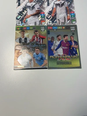 FIFA 365 Adrenalyn samlarkort - Fyra olika FIFA 365 Adrenalyn samlarkort med fotbollsspelare i olika lagtröjor. Två kort med tyska landslagsspelare i vita matchställ och två holografiska Invincible-kort med spelare från olika europeiska klubbar. Perfekt för dig som gillar att samla på fotbollskort.