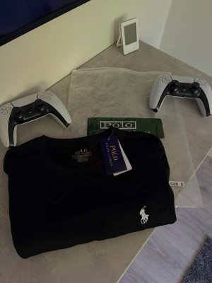 Svart t-shirt från Polo Ralph Lauren - Klassisk svart t-shirt från Polo Ralph Lauren med den ikoniska vita hästloggan broderad på bröstet. T-shirten har rund halsringning och korta ärmar. Tillverkad i mjuk bomull för en skön och stilren look.
