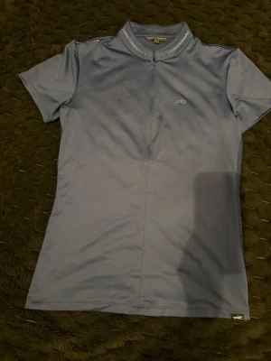 Blå funktions-tshirt från JH Collection - Snygg blå t-shirt från JH Collection med korta ärmar och hög krage. Tillverkad i ett stretchigt material som sitter tight mot kroppen. Dekorativ söm längs framsidan och diskret logga på bröstet. Perfekt för dig som gillar stilrena plagg med sportig känsla.