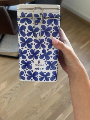 Blåvit kaffeburk Rörstrand Zoégas - Snygg kaffeburk i metall från Rörstrand i samarbete med Zoégas. Burken är vit med blått blommönster och har ett praktiskt metallspänne för att hålla locket på plats. Perfekt för förvaring av kaffe eller andra torrvaror i köket.  HELT NY! Buda gärna