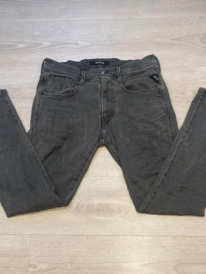 Gråa Replay jeans med smal passform - Säljer ett par gråa jeans från Replay med smal passform och klassisk femficksdesign. Jeansen har svarta detaljer, Snygg Replay-logga på bakfickan och patch i läder bak i midjan. Materialet är mjukt denim med lätt tvättad look.