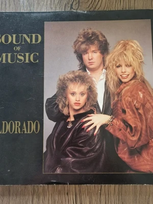 Sound of Music - Eldorado vinylsingel - Vinylsingel med gruppen Sound of Music, låtarna 'Eldorado' och 'West Indies Nights'. Omslaget har svart bakgrund med bild på bandmedlemmarna och guldfärgad text. Producerad av Peter Grönvall och Jörgen Appelgren. Perfekt för dig som gillar 80-talsmusik och samlar på vinyl.