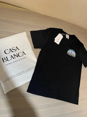 Svart Casa Blanca t-shirt med tryck - Snygg svart t-shirt från Casa Blanca med färgglatt tryck på bröstet och stort motiv på ryggen. T-shirten har rund hals och korta ärmar. Perfekt för dig som vill sticka ut med en unik design och coolt märke.