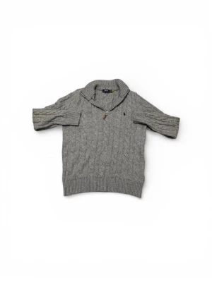 Grå kabelstickad tröja Polo Ralph Lauren - Kabelstickad grå tröja från Polo Ralph Lauren med halv dragkedja och liten broderad logga på bröstet. Tröjan har ribbade muddar, kortare ärmar och hög krage. Perfekt för lager på lager och en chill look.