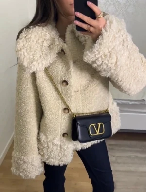 Beige teddyjacka med stora knappar - Supermysig beige teddyjacka med oversized passform och stora bruna knappar framtill. Jackan har bred krage och fluffigt, mjukt material som ger en trendig look. Perfekt för kyliga dagar när du vill vara både varm och snygg.