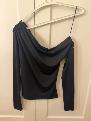 Svart offshoulder topp med lång ärm - Svart offshoulder topp från H&M med långa ärmar och draperad effekt över axlarna. Toppens material är stretchigt. Använd endast ett fåtal gånger.