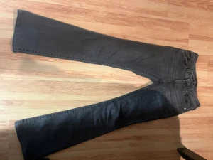 Mörkgrå mid rise bootcut jeans True Religion - Snygga mörkgrå bootcut jeans från True Religion med detaljerade bakfickor med knappar. Dom är använda men är ett bra skick. De är lite slitna längs ner bak vid benen. St. 24