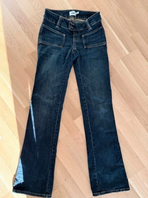 Mörkblå bootcut jeans från 157 - Snygga mörkblå bootcut jeans från 157 med dubbla knappar i midjan och raka, lätt utsvängda ben. Jeansen har stora framfickor och kontrastsömmar som ger en cool retrovibe. Perfekta för dig som gillar en avslappnad men trendig stil.