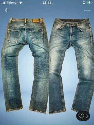 Blå slitna jeans från Nudie Jeans - Säljer ett par blå jeans från Nudie Jeans med snyggt slitna detaljer och klassisk femficksmodell. Jeansen har raka ben, normal midja och tydliga slitningar framtill och baktill för en cool vintage-look. Perfekta för dig som gillar streetwear. Även i denim