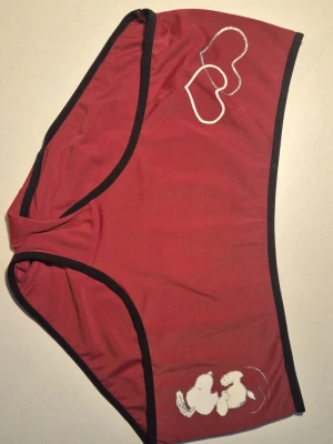 Röda trosor med Snoopy-tryck Strl Large - Säljer ett par röda trosor med svarta kanter och tryck av Snoopy samt två vita hjärtan framtill. På baksidan står det 'SNOOPY' i vitt. Materialet känns mjukt och stretchigt, perfekt för dig som gillar bekväma och lekfulla underkläder.