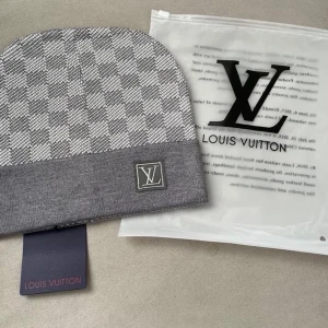 Grå mössa med rutmönster - Snygg grå mössa från med klassiskt rutmönster och vikt kant. Märkets ikoniska logga är broderad framtill. Tillverkad i mjukt material som känns skönt mot huden. Perfekt accessoar för att lyfta din outfit.