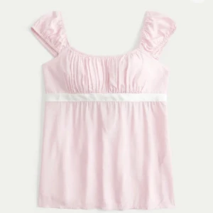 Ljusrosa topp med volangärmar och band - Supersöt ljusrosa topp med volangärmar och breda axelband. Toppen har en vit satinliknande rosett under bysten som kan knytas i ryggen. Perfekt för dig som gillar romantisk och feminin stil. S/XS 