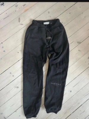 Svarta Essentials mjukisbyxor - Svarta mjukisbyxor från Essentials med snörning i midjan och resår vid bensluten. Byxorna har en enkel och clean look med diskret logga på benet. Perfekta för chill dagar eller när du vill vara bekväm.