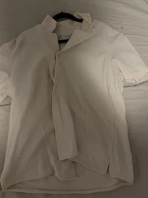 Vit kortärmad skjorta från Zara - Säljer en vit kortärmad skjorta från Zara med klassisk krage och knäppning framtill. Skjortan är tillverkad i ett mjukt tyg som känns skönt mot huden och har en avslappnad passform. Perfekt för en clean och enkel stil.