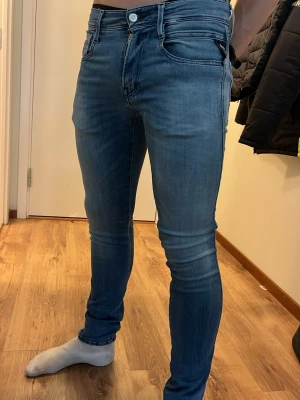 Replay anbass - Snygga blå slim fit jeans med stretch som sitter tight över benen. Klassisk femficksmodell med dragkedja och knapp i midjan. Jeansen har diskreta slitningar och detaljerade bakfickor. Perfekta för dig som gillar en modern och smal siluett.