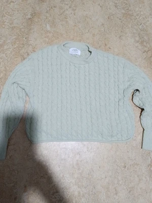 Ljusgrön kabelstickad tröja Zara - Ljusgrön kabelstickad tröja från Zara med rund halsringning och långa ärmar. Tröjan har ett klassiskt flätmönster och ribbade muddar vid ärmslut och nederkant. Perfekt för dig som gillar en enkel men snygg stil.