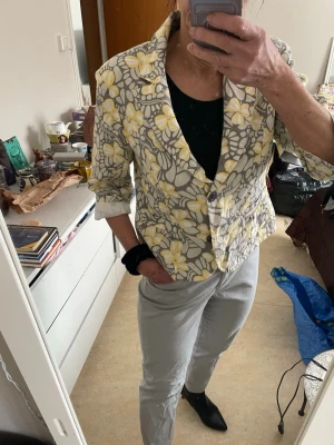  80-tal Retro KavajBlommig kavaj från flash - 80-tal Retro KavajBlommig kavaj från flash.med grå och vita blommor samt gula detaljer. Kavajen har två knappar framtill, klassisk krage och trekvartsärmar med uppvik. Perfekt för dig som vill sticka ut med ett färgglatt mönster. Materialet känns lätt och passar till många olika stilar.