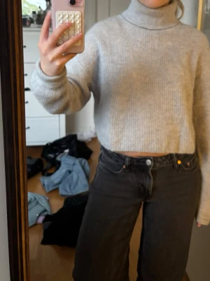 Ljusgrå croppad polotröja stickad - Mysig ljusgrå stickad polotröja med croppad passform och långa ärmar. Tröjan har ribbstickad struktur och hög polokrage, perfekt för lager på lager. Materialet ser ut att vara en mjuk ull- eller akrylblandning. Enkel och stilren design som passar till det mesta.