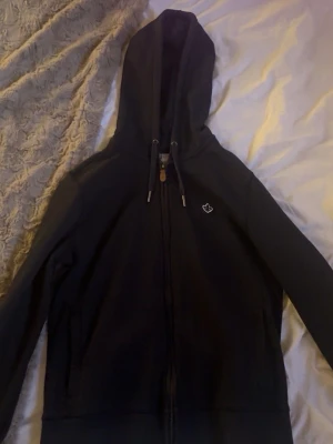 Mörkblå hoodie från Morris - Mörkblå zip-hoodie från Morris med en liten broderad logga på bröstet. Klassisk modell med fickor framtill och mjukt material som känns skönt mot huden. Perfekt för en avslappnad och sportig stil. I princip i nyskick. Köpt för någon sommar sen men passar inte längre så har bara legat i garderoben. Ny pris låg på ca 1100kr.