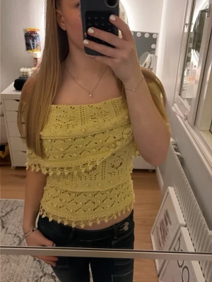 Gul offshoulder stickad topp - Snygg gul stickad offshoulder topp med fransar och dekorativa detaljer. Perfekt för dig som vill ha en unik och trendig look. Toppens stickade struktur och fransar ger en bohemisk känsla och den är croppad för en modern stil.
