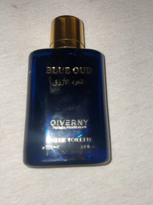 Blue Oud parfym från Giverny - Blue Oud från Giverny är en elegant parfym i en djupblå glasflaska med guldfärgat lock. Flaskan har en stilren, rektangulär form och text i guld på framsidan. Doften är inspirerad av oud och ger en lyxig känsla.