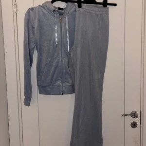 Ljusblå velour loungewear-set - Mysigt loungewear-set i ljusblå velour med zip-hoodie och matchande byxor med dragsko i midjan. Hoodien har fickor och glänsande band i huvan. Perfekt för chill dagar hemma. L på byxa M på tröja