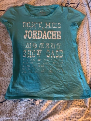 Turkos Jordache t-shirt med tryck - Snygg turkos vintage  t-shirt från Jordache med stort vitt tryck på framsidan där det står 'DON'T MISS JORDACHE MOMENT SHOW CASE'. T-shirten har rund halsringning och korta ärmar. Tillverkad i mjuk bomull för en skön känsla. Storlek L men liten i storleken.
