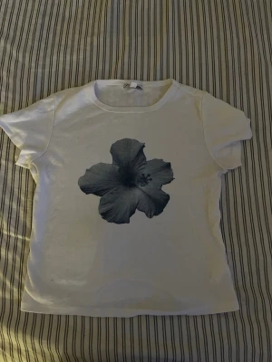 Vit t-shirt från subdued - Vit t-shirt med en mörkblå blomma på. Rund halsringning och korta ärmar. Jätte cute o simpel tröja. Har bara haft den två gånger. Fin men vill bara inte ha längre. 