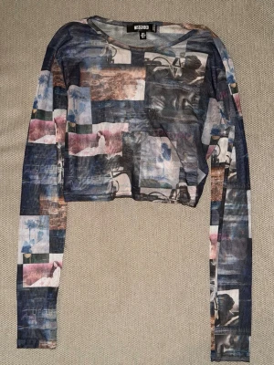 Croppad mesh-topp från Missguided - Trendig croppad mesh-topp från Missguided med lång ärm och coolt fotoprint i blå, grå, rosa och bruna toner. Tunn och lätt, perfekt att styla lager på lager. Rund halsringning och figurnära passform.