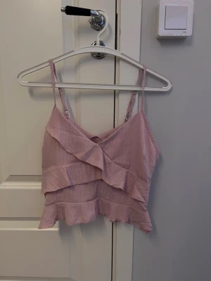 Rosa linne - Ett fint rosa linne med volanger. Storlek S och kort i storleken, aldrig använt men väldigt fint. 