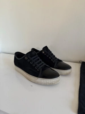 Svarta lanvins Cap Toes - Snygga svarta sneakers från Lanvin med ovandel i mocka och tåparti i blankt lack. Klassisk låg modell med vita sulor och svarta skosnören. Något använda skosulorna enligt bilderna. Perfekta för dig som gillar stilrena och exklusiva sneakers. Dust bag ingår även. Innermåttet är 26,5cm och passar mer 41-42. Seriösa köpare hör av er till mig vid funkeringar!