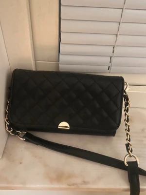 Svart Don Donna Väska - Snygg svart axelväska från Don Donna med quiltat mönster och guldfärgade detaljer. Väskan har en kedjerem i kombination med läder och en stilren, rektangulär form. Perfekt för att lyfta din outfit med en trendig touch. Bandet är avtagbart. Knappt använd och säljer pga för många väskor 😊