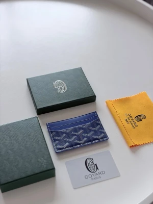 Goyards plånbok blå - Snygg blå korthållare med ikoniskt mönster i vitt och grått. Tillverkad i exklusivt läder med flera kortfack och elegant logotyp framtill. Perfekt för dig som vill ha en stilren och lyxig accessoar i fickan.